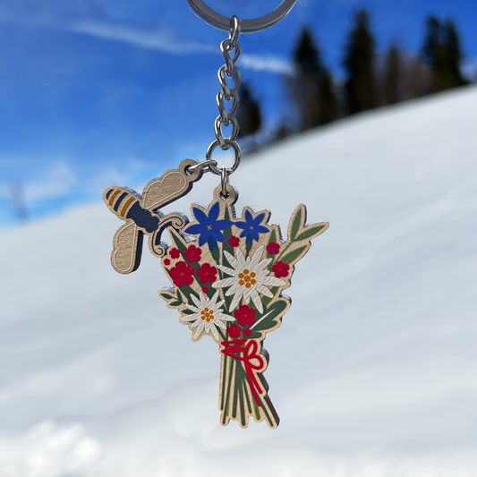 Keychain with alpine floral design and bumblebee charm against a snowy landscape
