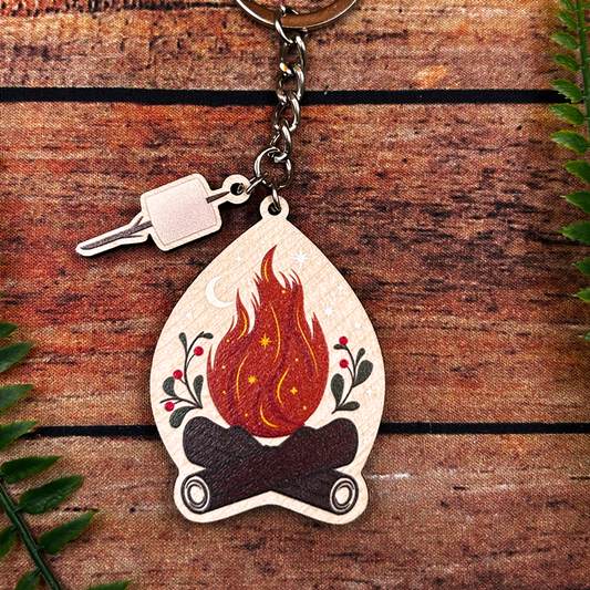 Keychain with a design of a campfire and logs on a wooden surface