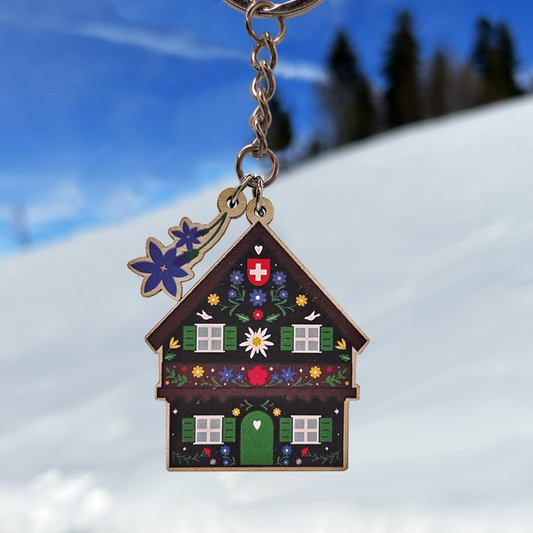 Keychain shaped like a decorated Swiss chalet with flowers against a snowy landscape