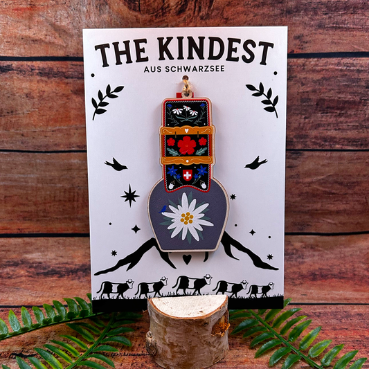 Decorative item on a card with 'The Kindest' branding against a wooden background