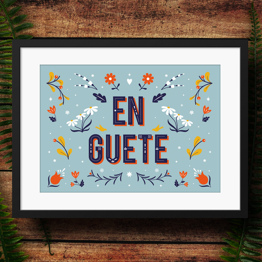 Framed artwork with 'EN GUETE' text and floral designs on a wooden surface