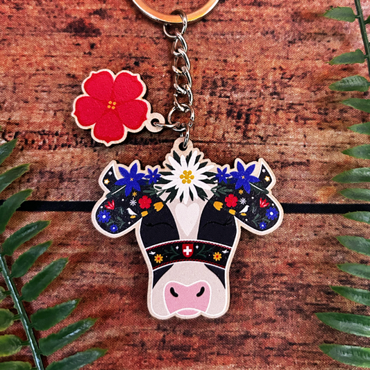 Keychain with cow design and floral elements on a wooden surface with leaves.