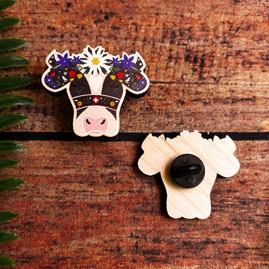 wooden pin badge of a holstein cow with flowers on its head in the swiss alpabzug style.