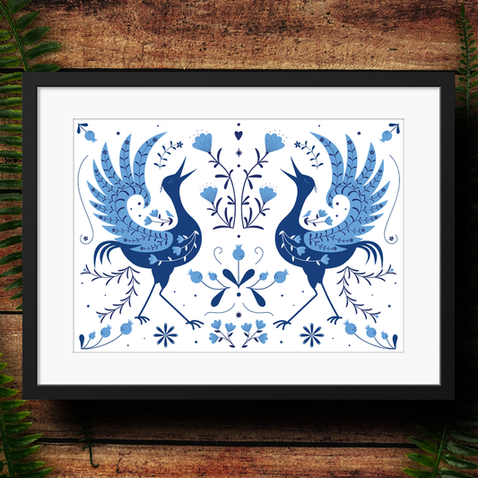 Framed artwork with blue illustrated herons on a white background, placed on a wooden surface.