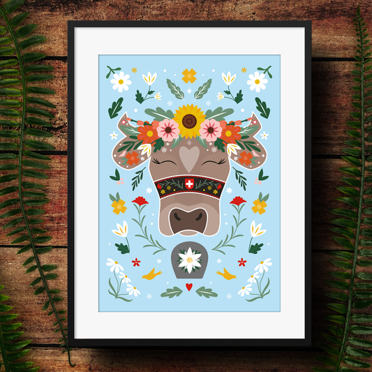 Framed artwork of a Swiss cow with flowers and patterns on a wooden surface with leaves.