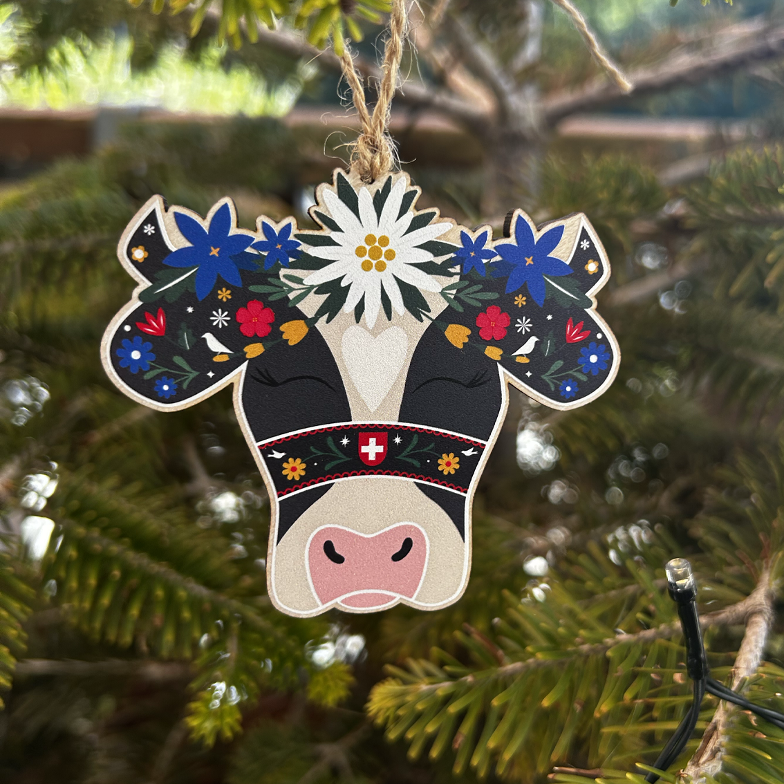 Decorative cow ornament with floral patterns hanging on a Christmas tree.