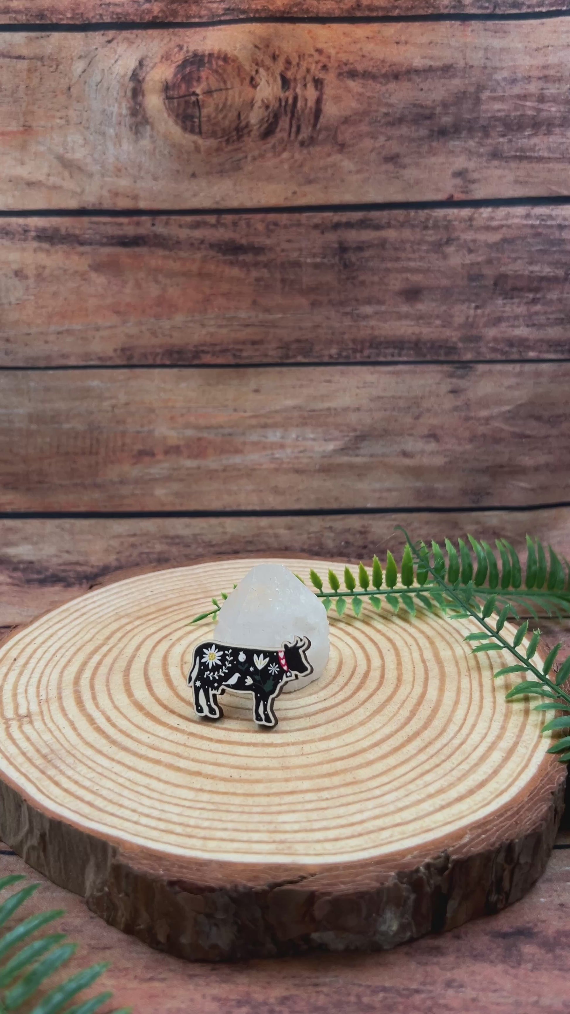 video showing illustrated black cow with flowers on wooden pin badge.