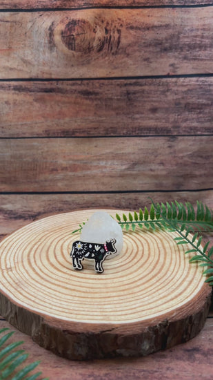 video showing illustrated black cow with flowers on wooden pin badge.